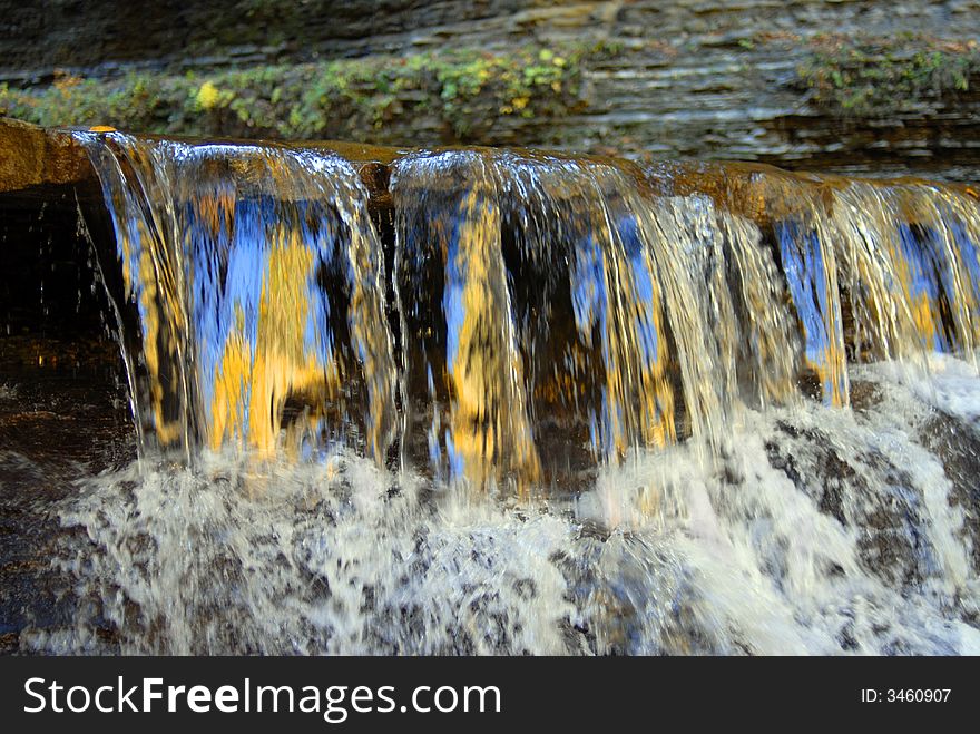 A brilliant blue sky and golden leaves reflected in the low waterfalls of a shallow brook. A brilliant blue sky and golden leaves reflected in the low waterfalls of a shallow brook.