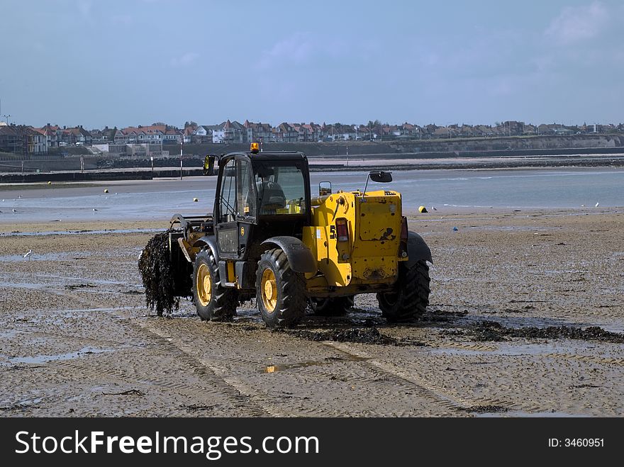 Beach Digger clearing seaweed from the beach right next to the sea with a blue sky.