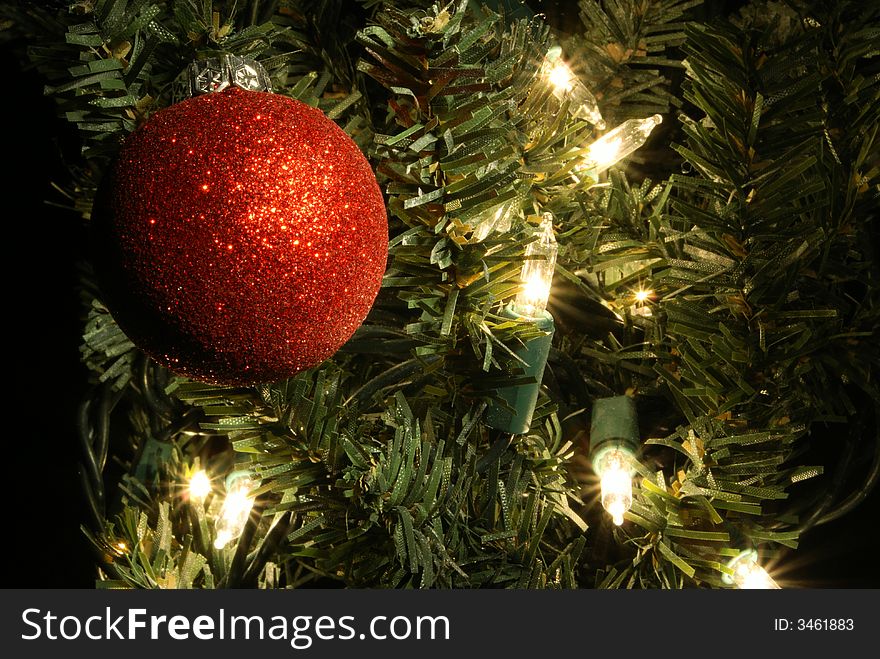 Glittery red christmas ball in lighted christmas tree. Glittery red christmas ball in lighted christmas tree