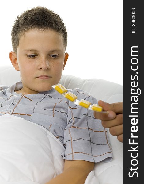 Young boy looking at yellow tablets. He's lying in the bed. White background. Young boy looking at yellow tablets. He's lying in the bed. White background