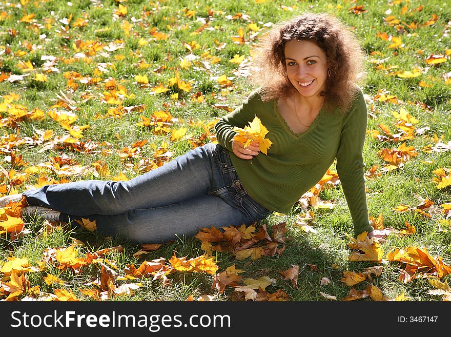 Woman with the yellow leaf sits on the grass