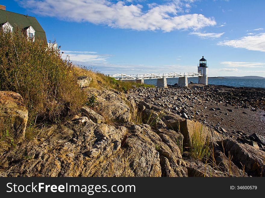 Looking at the Marshall Point lighthouse from a low perspective in the rocks on the shore.