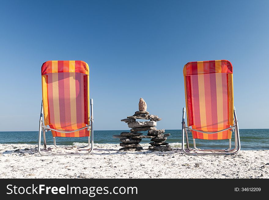 To chairs at the beach facing onto Lake Ontario with a stone formation between the chairs