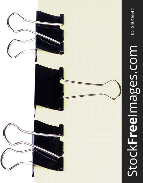 Black Metal Paper Clip In a Row on Checkered Yellow Paper isolated on white background. Black Metal Paper Clip In a Row on Checkered Yellow Paper isolated on white background