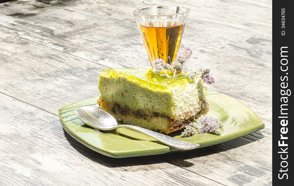 Slice of lime cheesecake decorated with mint flowers and glass of cognac