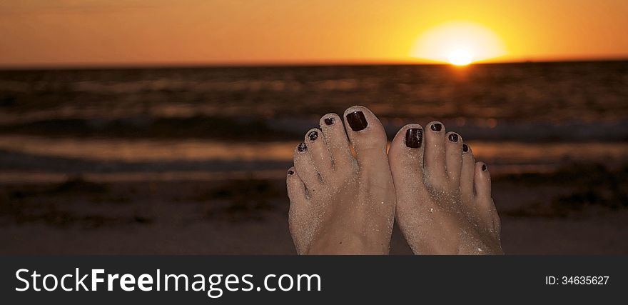 Womens feet with painted toe nails with a beautiful beach sunset in the background. Womens feet with painted toe nails with a beautiful beach sunset in the background