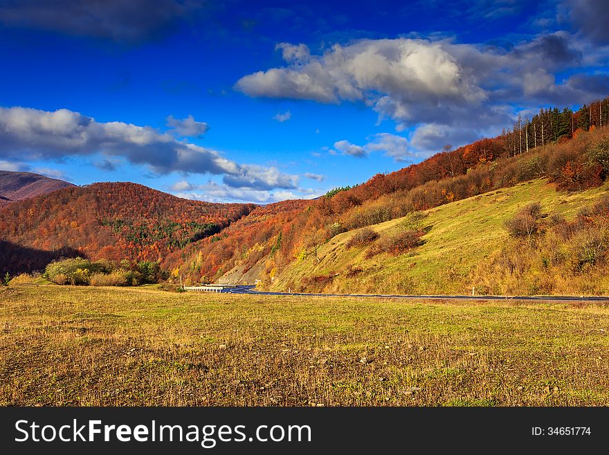 Autumn mountain landscape. S-curve road in the morning at the foot of the mountain. on the mountain forest with red and yellow leaves. Autumn mountain landscape. S-curve road in the morning at the foot of the mountain. on the mountain forest with red and yellow leaves