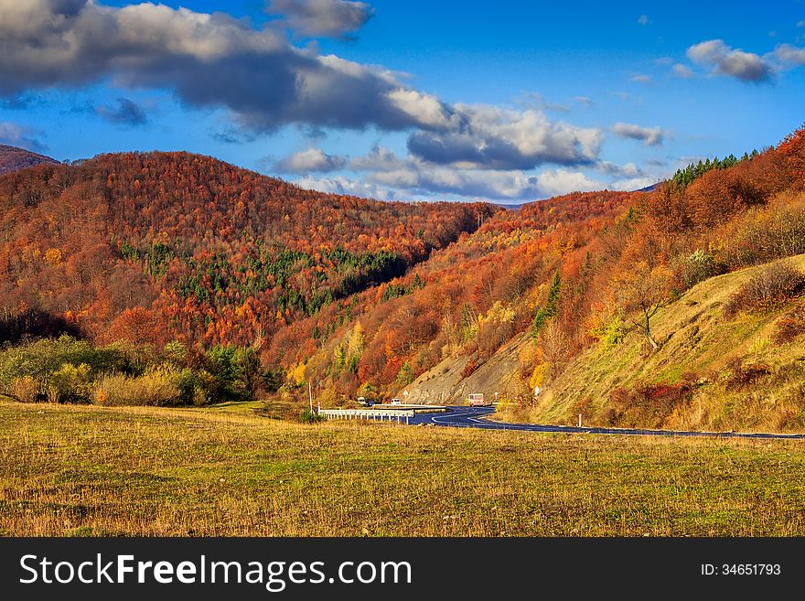 Autumn mountain landscape. S-curve road in the morning at the foot of the mountain. on the mountain forest with red and yellow leaves. Autumn mountain landscape. S-curve road in the morning at the foot of the mountain. on the mountain forest with red and yellow leaves