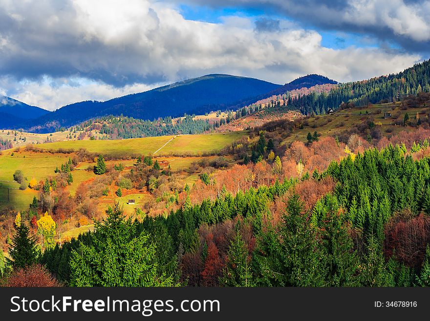 Autumn landscape. forest on a hillside covered with red and yellow leaves. over the mountains against blue sky clouds. Autumn landscape. forest on a hillside covered with red and yellow leaves. over the mountains against blue sky clouds