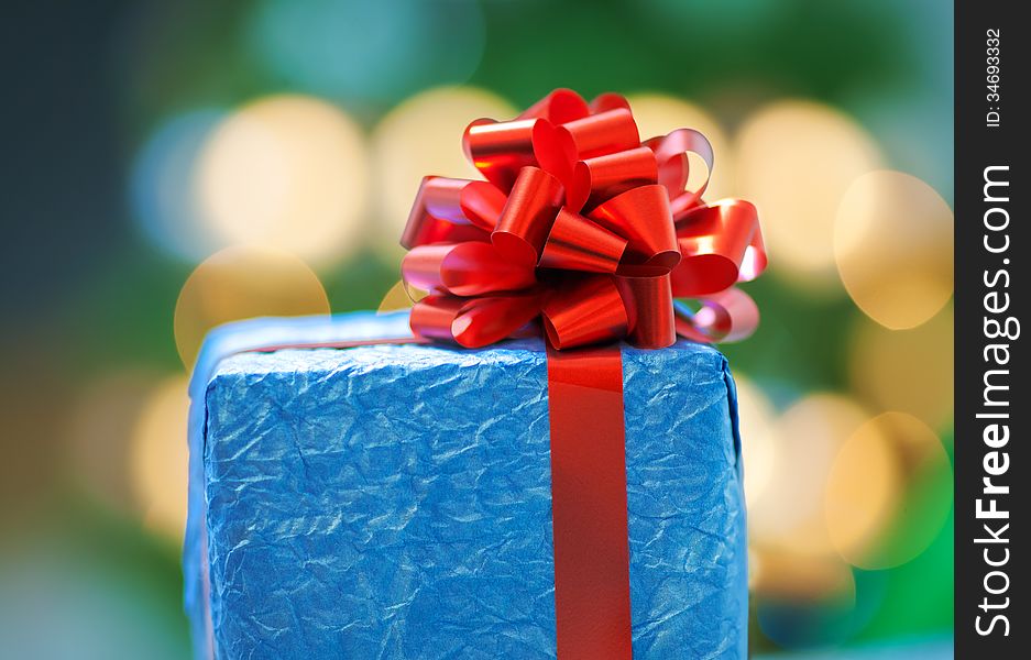 A blue gift with a red ribbon on Christmas bokeh background