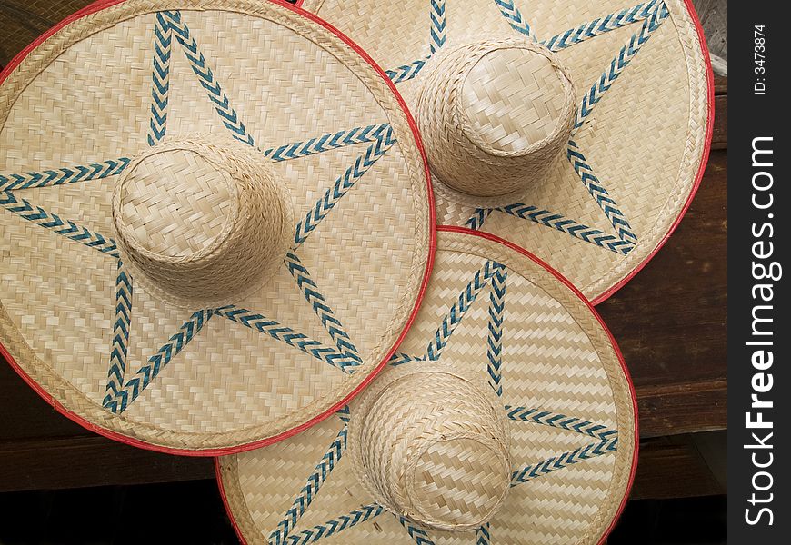 Three large, sombrero-style straw-hats, on a dark, wooden background