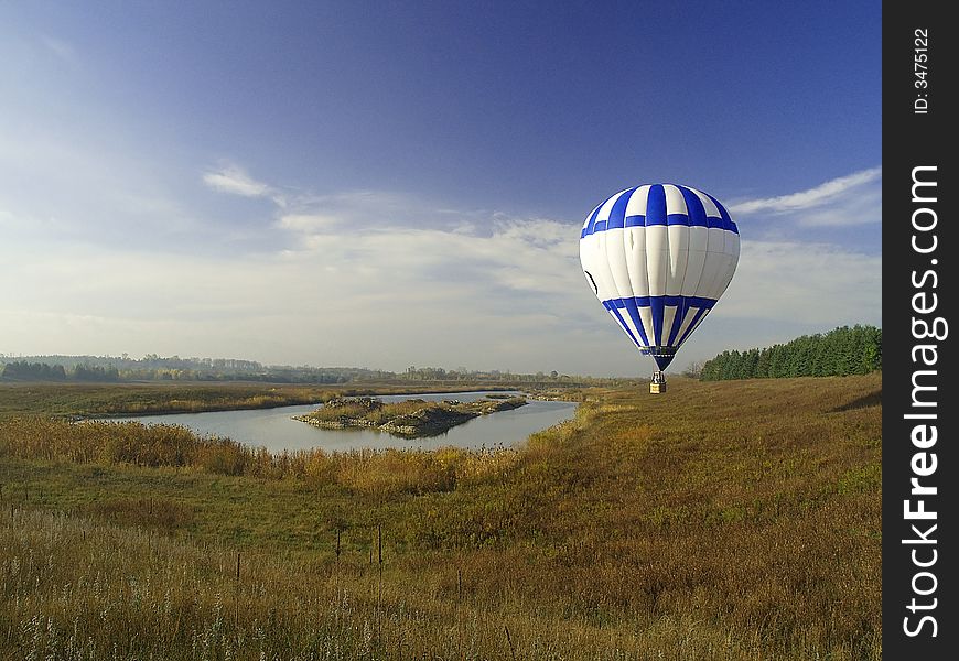 A blue and white hot air balloon hovers near a pond. A blue and white hot air balloon hovers near a pond.