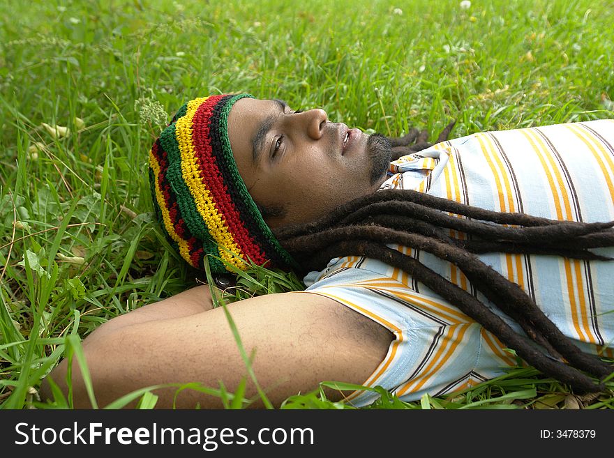 Sad Rastafarian Jamaican thinking laid on grass. Sad Rastafarian Jamaican thinking laid on grass