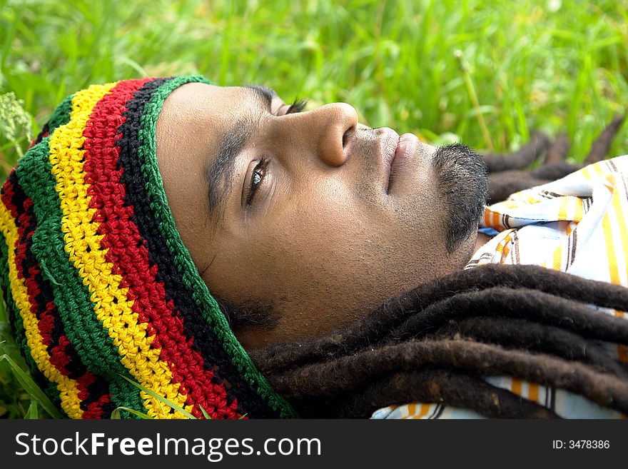 Sad Rastafarian Jamaican thinking laid on grass. Sad Rastafarian Jamaican thinking laid on grass