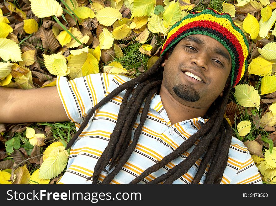 Happy Rastafarian Jamaican smiling laid on yellow leafs. Happy Rastafarian Jamaican smiling laid on yellow leafs