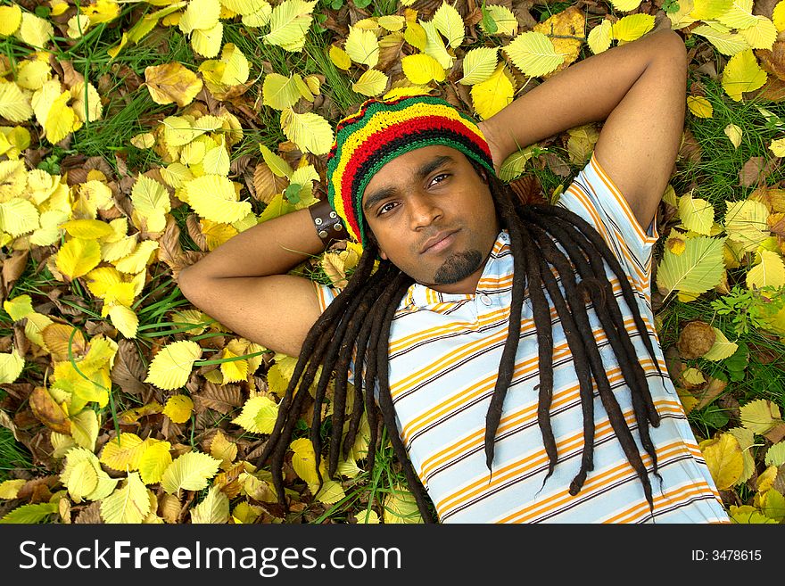 Happy Rastafarian Jamaican laid on yellow leafs. Happy Rastafarian Jamaican laid on yellow leafs