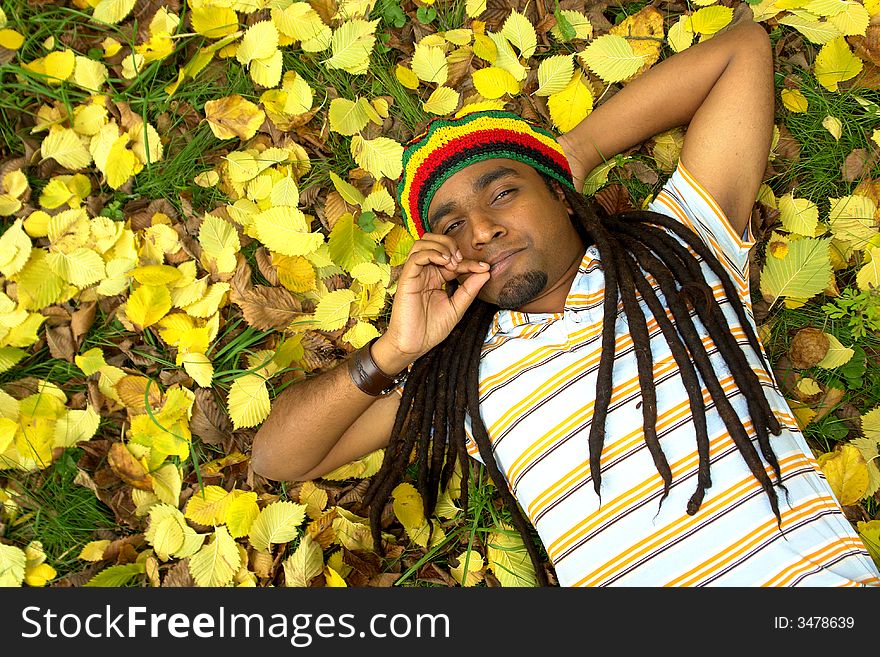 Happy Rastafarian Jamaican smiling laid on yellow leafs. Happy Rastafarian Jamaican smiling laid on yellow leafs