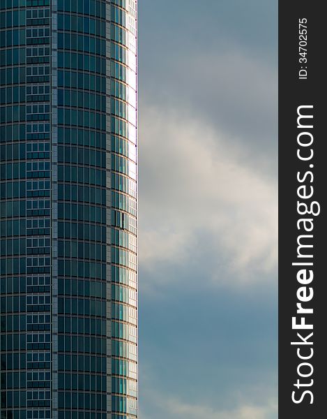 Rounded Tall Skyscraper with Green Glass against Cloudy Stormy Sky. Rounded Tall Skyscraper with Green Glass against Cloudy Stormy Sky