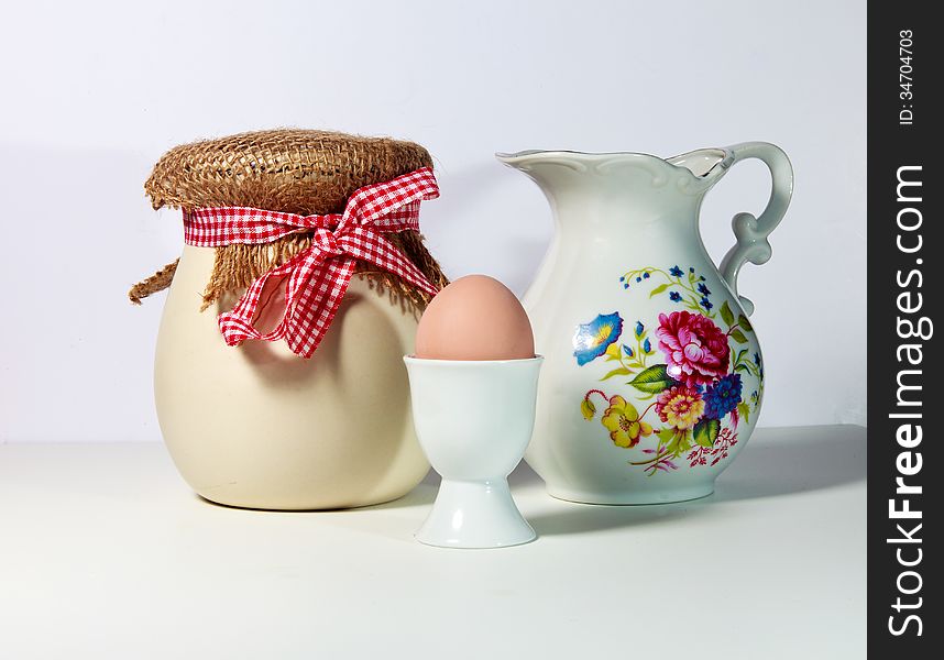 An arrangement of a jar, pitcher and egg in egg cup on white background. An arrangement of a jar, pitcher and egg in egg cup on white background