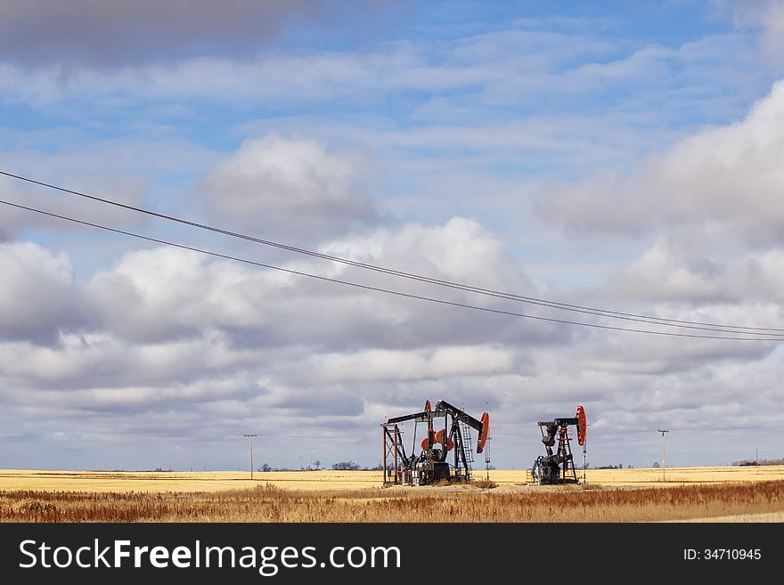 Two oil drills on harvested farmland under a cloudy sky. Two oil drills on harvested farmland under a cloudy sky