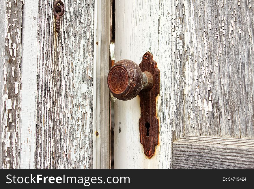 A rusted doorknob with a metal plated keyhole on a weathered white and grey door. A rusted doorknob with a metal plated keyhole on a weathered white and grey door