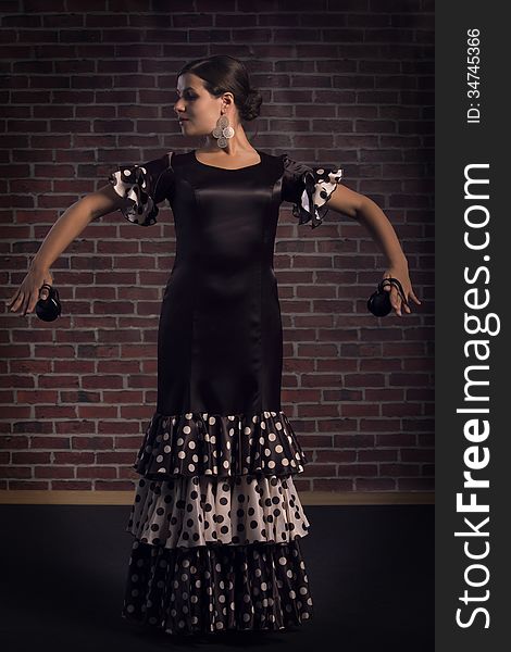 Young woman in beautiful dress performs Spanish dance with castanets. Red brick wall background. Young woman in beautiful dress performs Spanish dance with castanets. Red brick wall background.