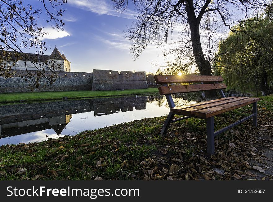 Sunset over the fortress of Fagaras and the swamp surrounding it with a bench from the park. Sunset over the fortress of Fagaras and the swamp surrounding it with a bench from the park