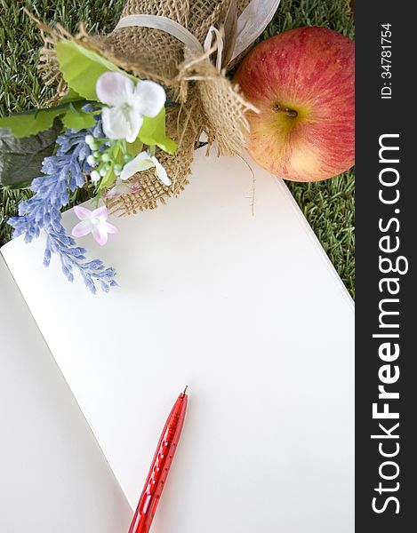 Blank white page with red pen and fresh apple on grass. Blank white page with red pen and fresh apple on grass