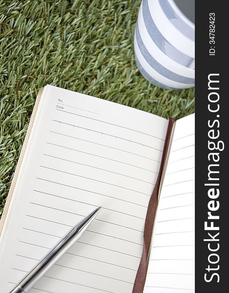 Open blank page of notebook with cup put on grass