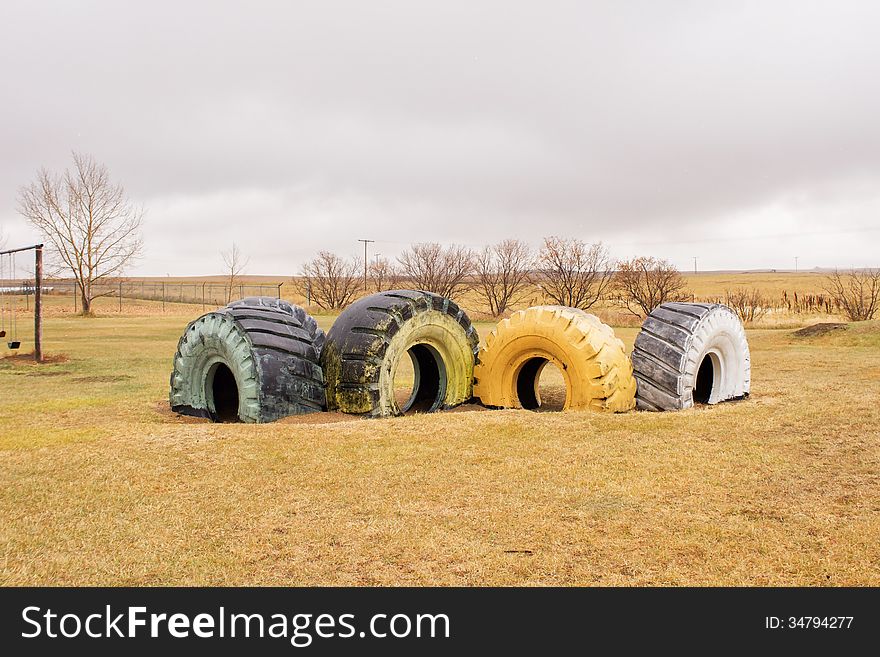 Four large painted tires in front of a few bare trees at a playground