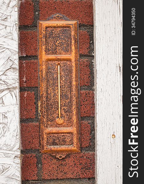 An old rusted thermometer on a fake brick wall