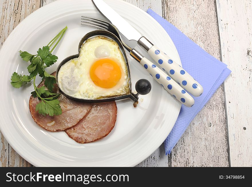 Modern breakfast of Ham with heart shape egg cooked breakfast on modern vintage shabby chic blue table with polka dot cutlery.