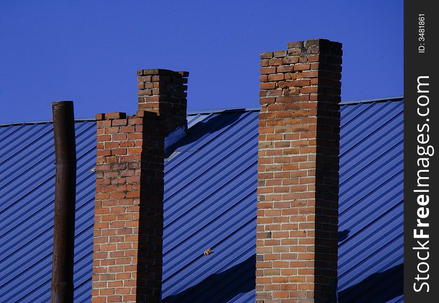 Four chimneys on a blue roof in front of a blue sky.