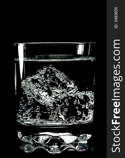 Ice cubes in glass of water with bubbles, isolated, black background