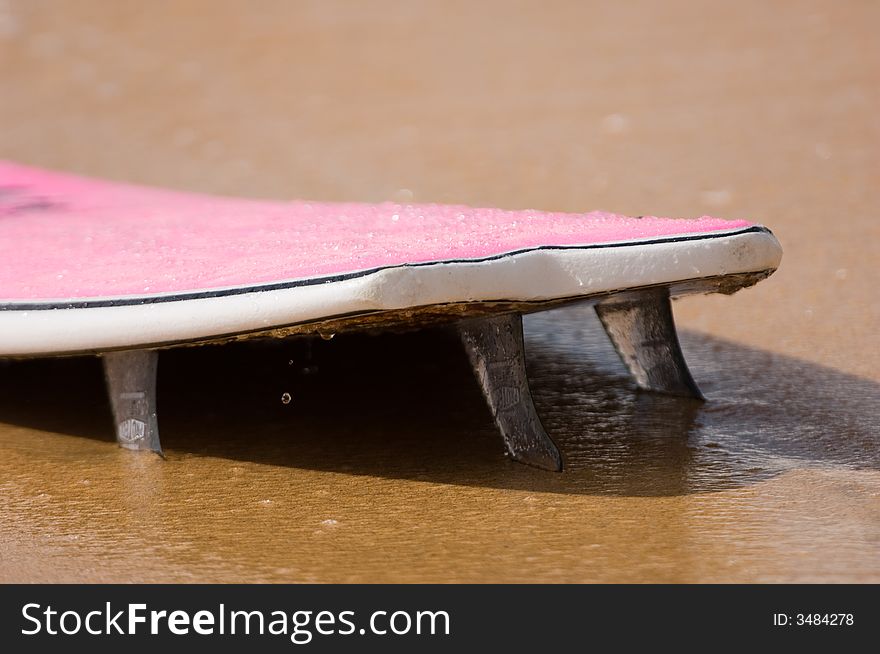 Pink surfboard washed up on the beach with fins stuck in the sand. Pink surfboard washed up on the beach with fins stuck in the sand