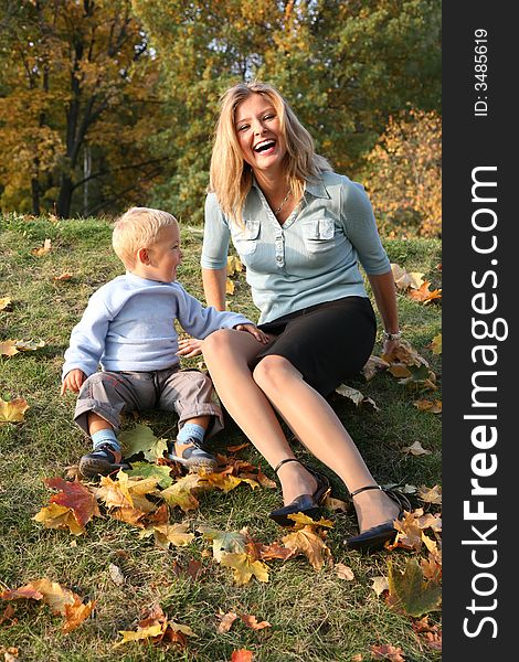 Blue-eyed blond sits with the son in the park in autumn. Blue-eyed blond sits with the son in the park in autumn