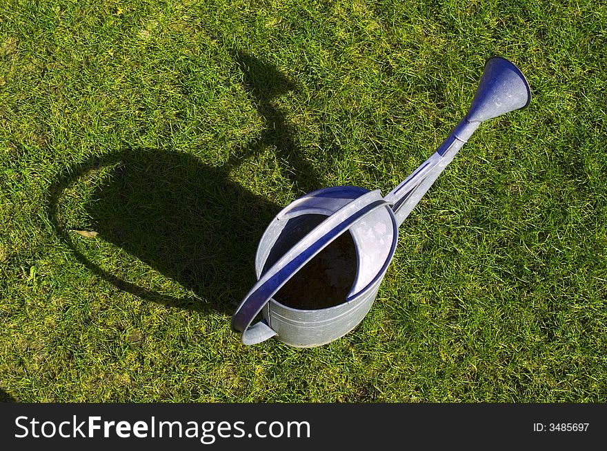 Empty watering-can on green grass with shadow