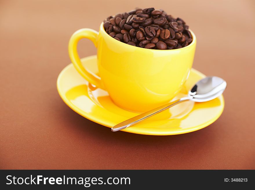 Yellow coffee cup filled with beans over a brown background