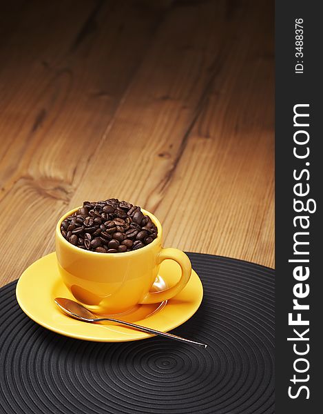 Yellow coffee cup filled with beans on a wooden table