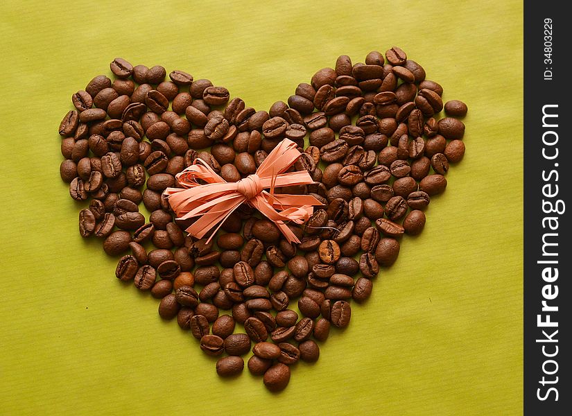 Photo of coffee beans in a shape of heart with a bow on green background