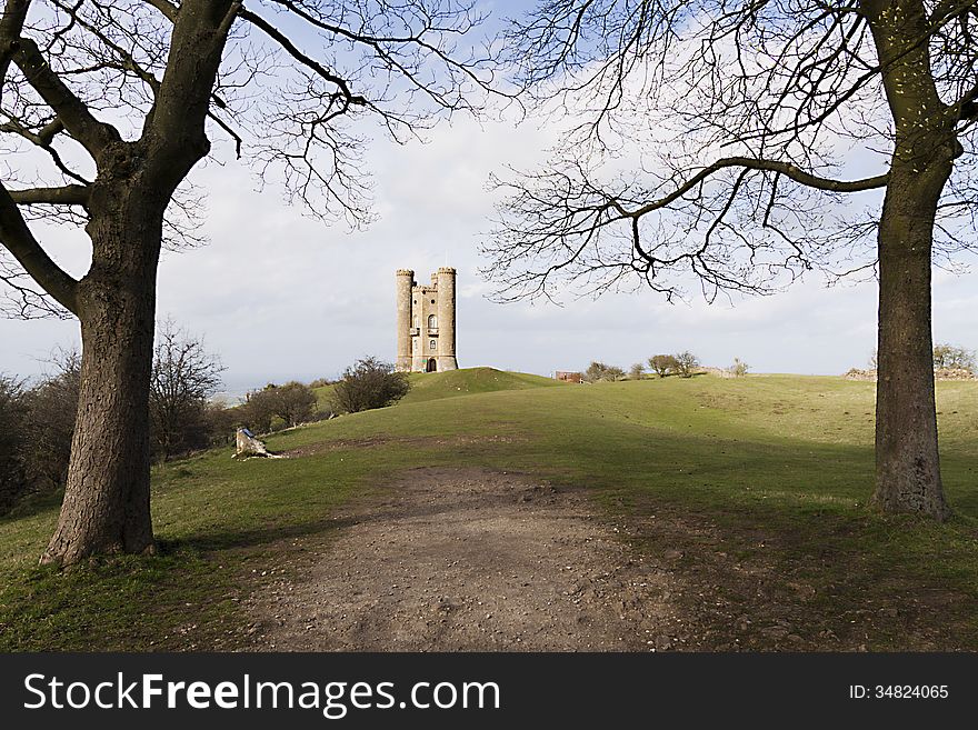 Broadway Tower is a folly located on Broadway Hill, near the village of Broadway in the Cotswolds UK. The image is framed by leafless trees on each side with a pathway leading to the Tower in the background. Broadway Tower is a folly located on Broadway Hill, near the village of Broadway in the Cotswolds UK. The image is framed by leafless trees on each side with a pathway leading to the Tower in the background