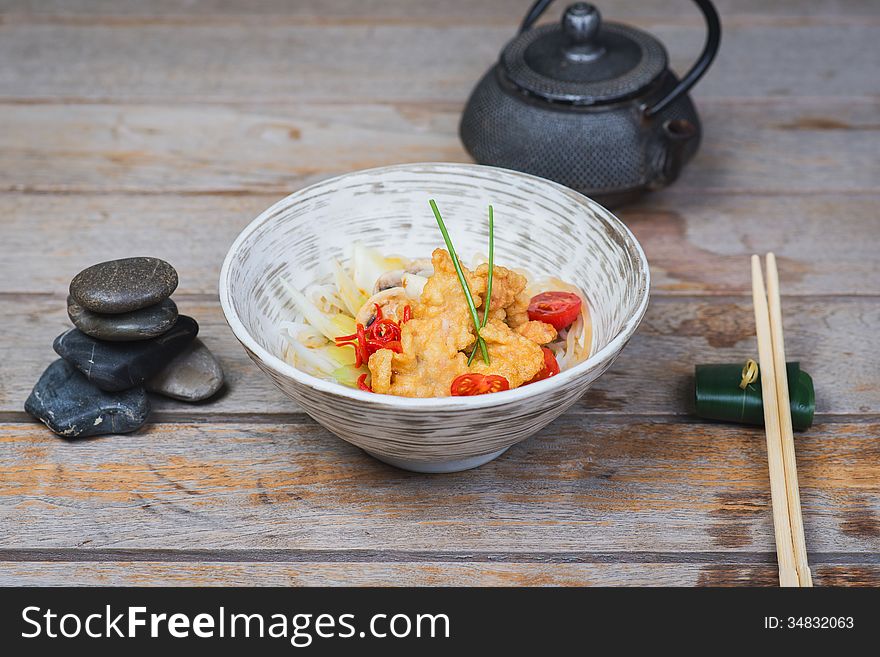 Tasty serving of Udon with chicken and cherry tomatoes on a wooden table in a restaurant. Tasty serving of Udon with chicken and cherry tomatoes on a wooden table in a restaurant