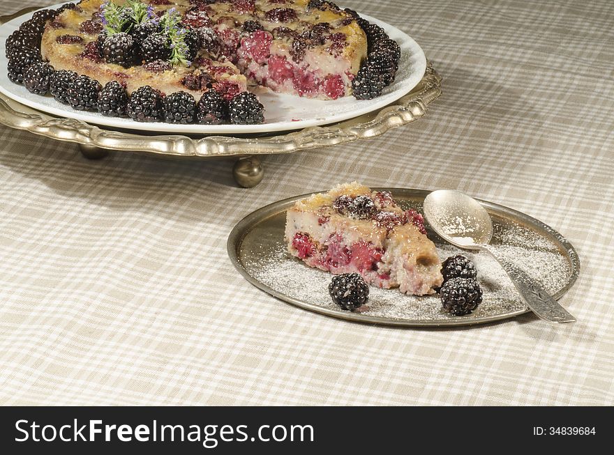 Slice of Blackberry Clafoutis on metal plate with fresh berries