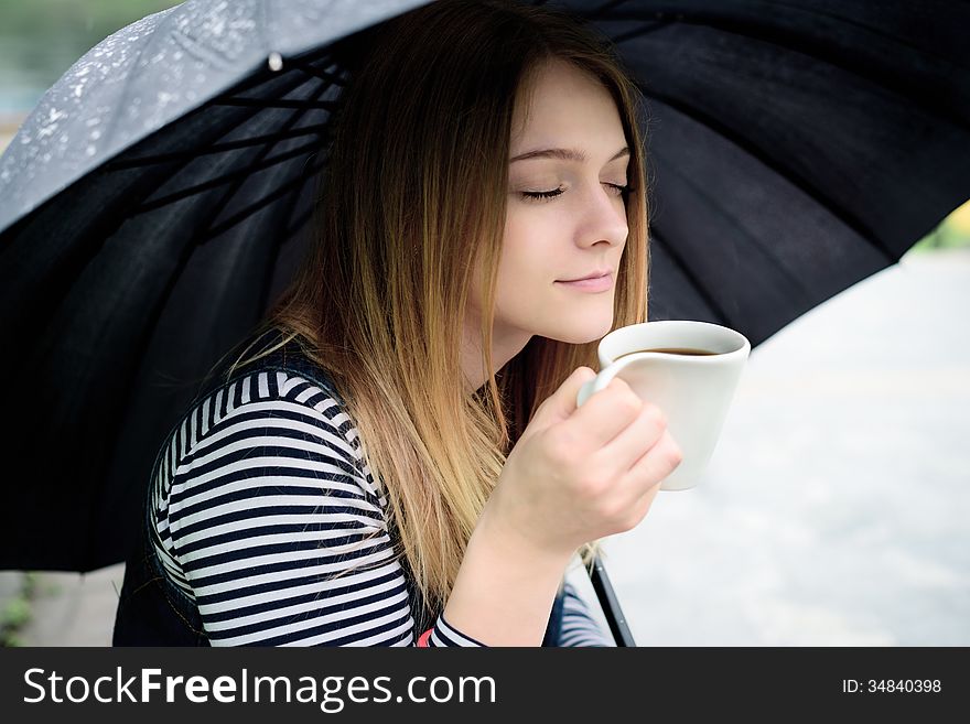 Womanl drinks fragrant coffee with pleasure under umbrella in bad weather