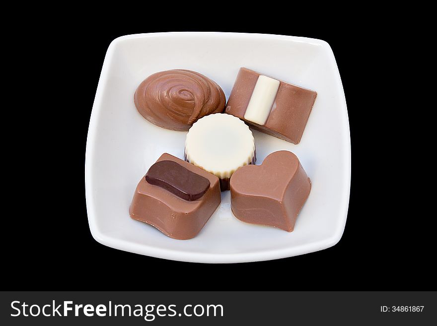 Cut-out of a variety of chocolates in a white plate over black background.