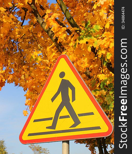 Road sign - beware of pedestrians - standing by the road on background of trees with leaves the color of autumn. Road sign - beware of pedestrians - standing by the road on background of trees with leaves the color of autumn.