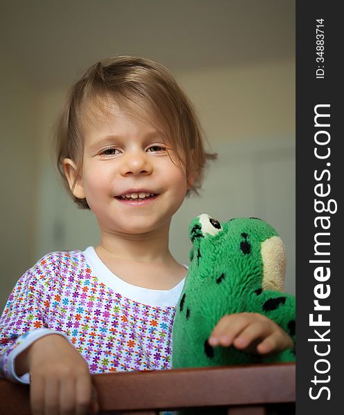 Cheerful little girl woke up in the morning, standing in the crib and keeps her toy. Cheerful little girl woke up in the morning, standing in the crib and keeps her toy