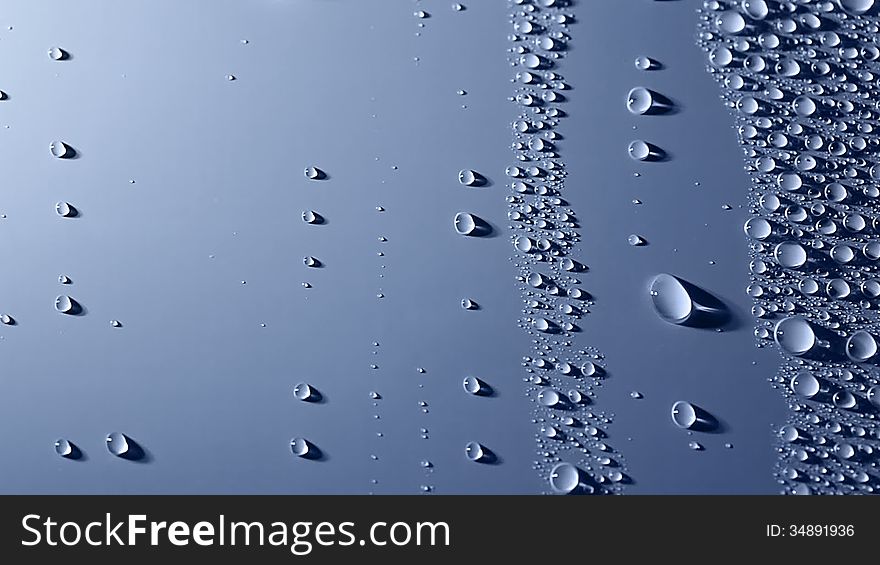 A lot of water drops are on the blue background. Oblique illumination. Shadows. Two large drops slowly slide down one after another. A lot of water drops are on the blue background. Oblique illumination. Shadows. Two large drops slowly slide down one after another