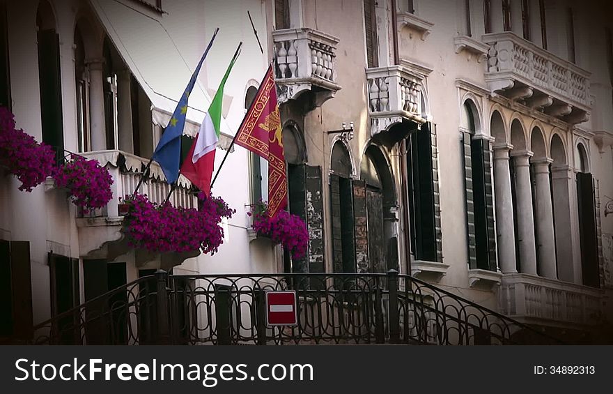 Venice. The narrow street. On the balcony of the building - the flowers and flags: the European Union, Italy and Venice. Venice. The narrow street. On the balcony of the building - the flowers and flags: the European Union, Italy and Venice