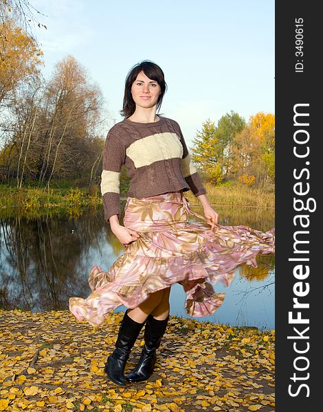 Young beautiful woman dancing at autumn park near small pond.